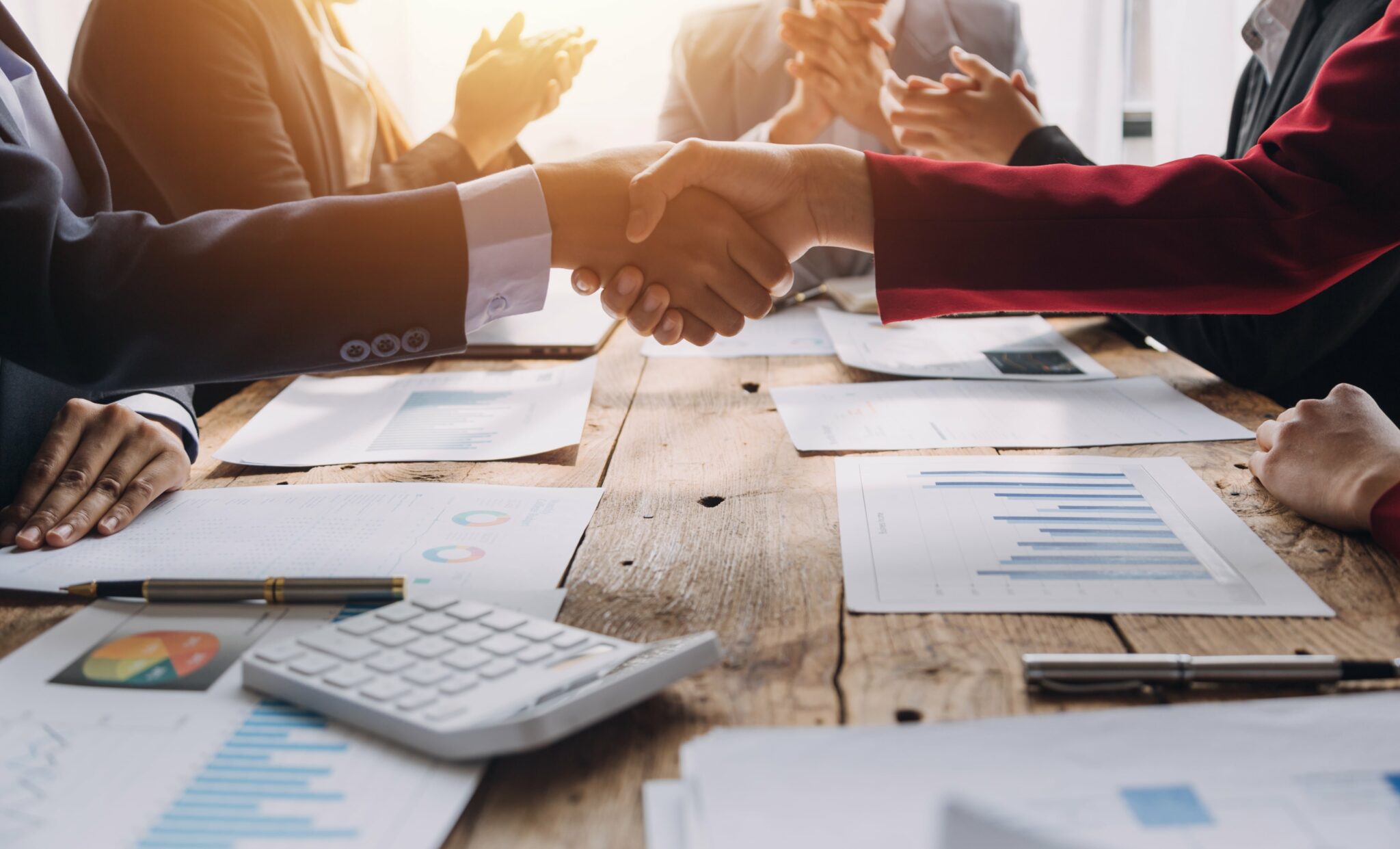 A handshake across a desk cluttered with papers and pens discussing company restructures|||Company restructures